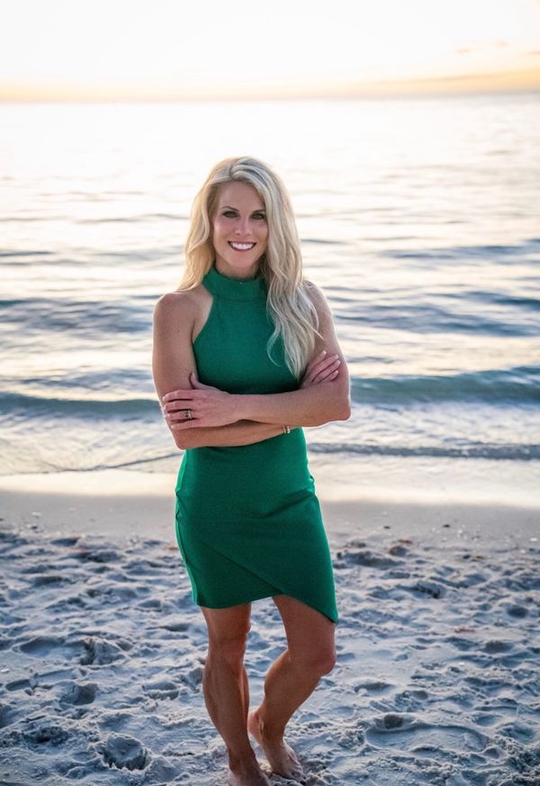 Kristy standing on the shore in a green dress, arms folded, smiling.